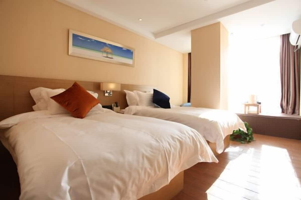 A hotel room with two beds, a painting on the wall, and a window with curtains.
