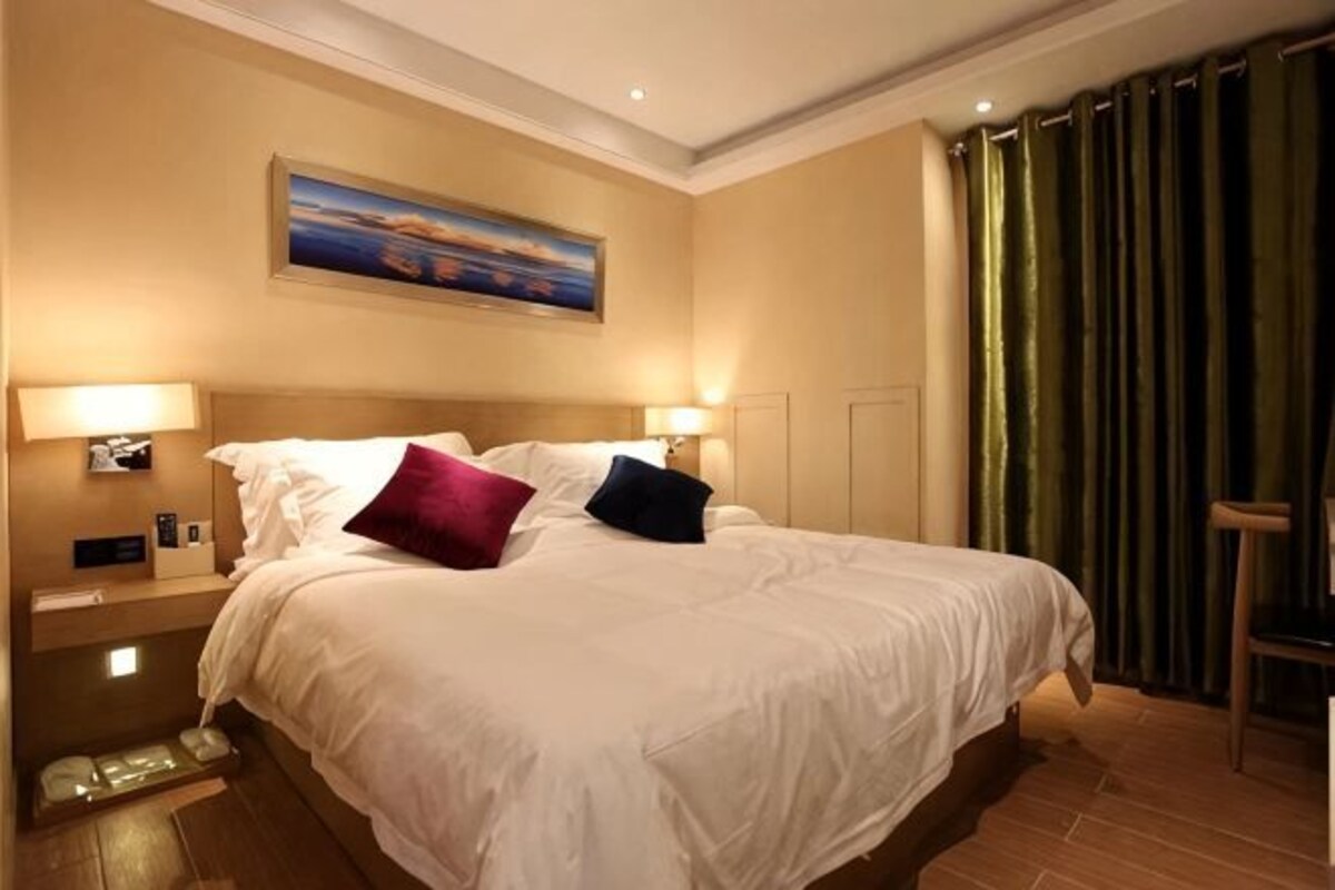 Una habitación de hotel con una cama grande, dos lámparas de noche, un cuadro en la pared y una cortina verde.