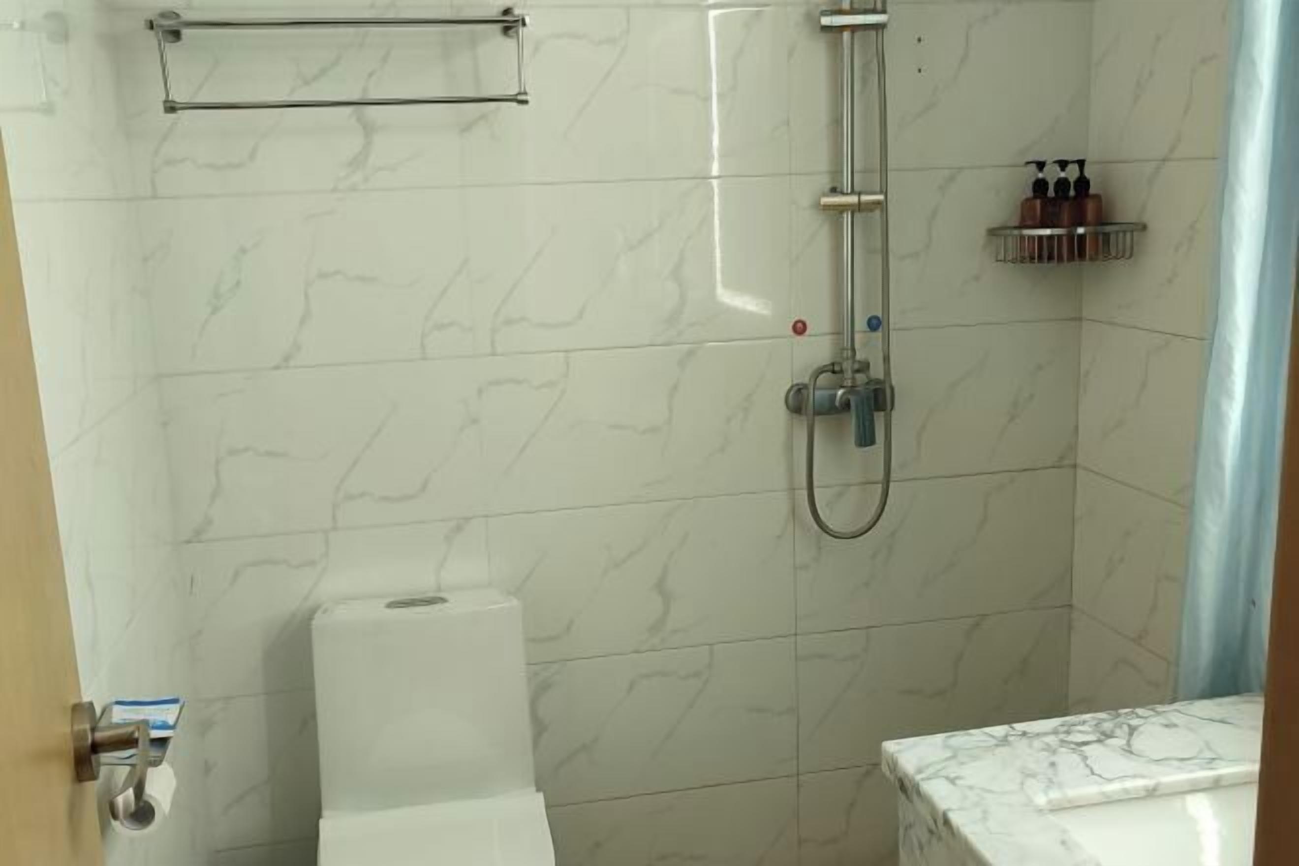 A bathroom with a shower, toilet, and marble-tiled walls.