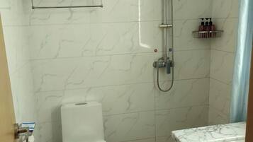 A bathroom with a shower, toilet, and marble-tiled walls.