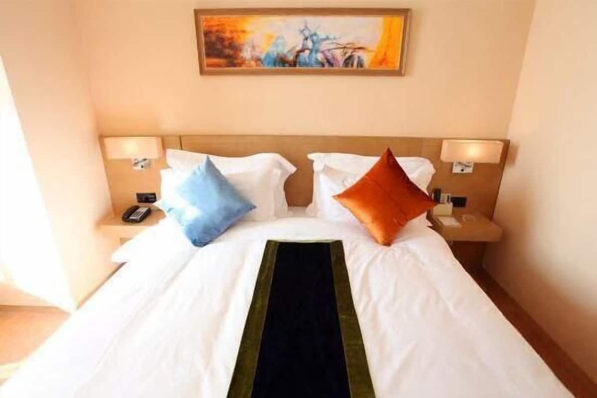 A hotel room with a large bed, two bedside tables, a painting on the wall, and a phone on one of the tables.