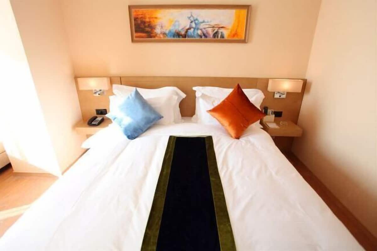 A hotel room with a large bed, two bedside tables with lamps, and a painting on the wall.