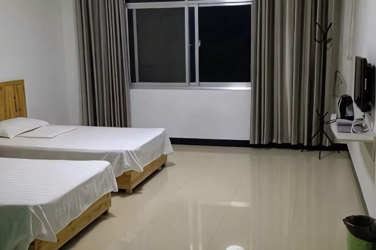 A hotel room with two beds, a window with curtains, a desk with a computer, and a trash bin.