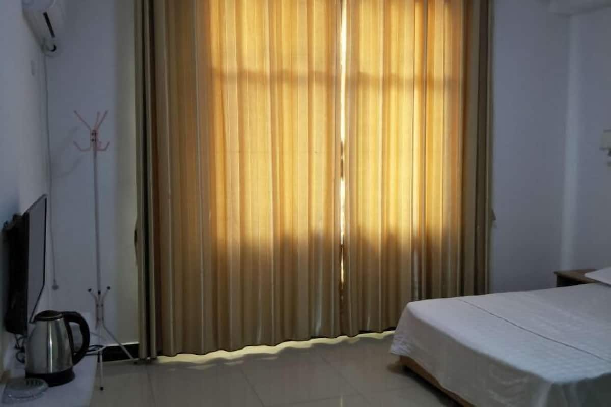 A hotel room with a bed, curtains, a television, and a kettle.