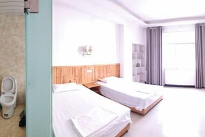 Habitación de hotel con dos camas individuales, cabecero de madera, inodoro blanco y un amplio ventanal con cortinas.