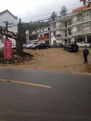 Un edificio con varios pisos y balcones, un estacionamiento con varios coches y un cartel.