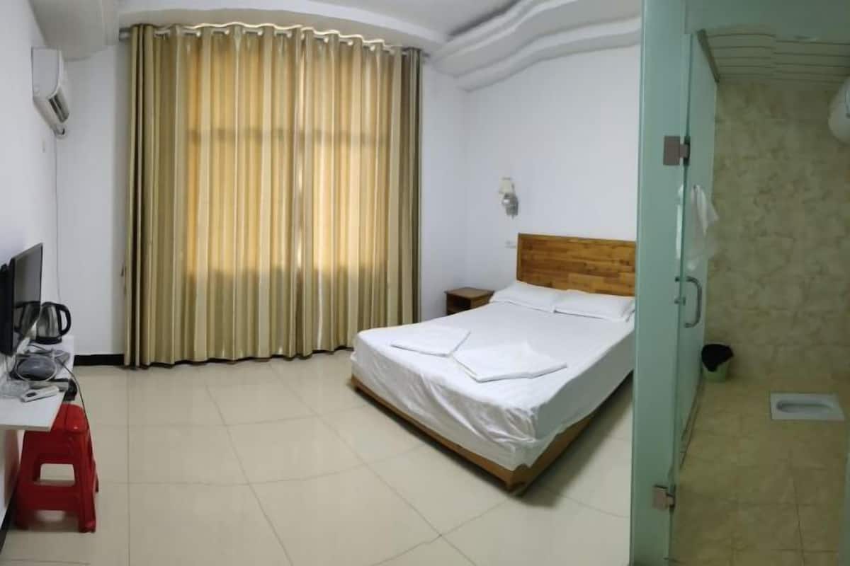 A hotel room with a bed, a desk with a chair, a television, and a window with curtains.