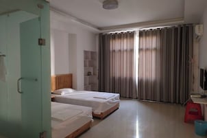 Habitación de hotel con dos camas, un escritorio, televisor, armario y ventana con cortinas.
