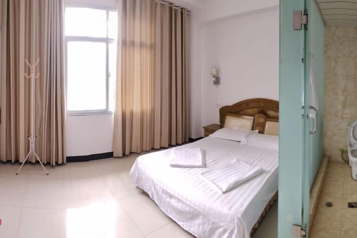 A hotel room with a bed, curtains, a bedside table, and a window.