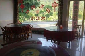 A restaurant interior with round tables and chairs, a glass partition, and a view of the outdoors. - Luotian Impression Hongye Mountain Villa (Luotian County)