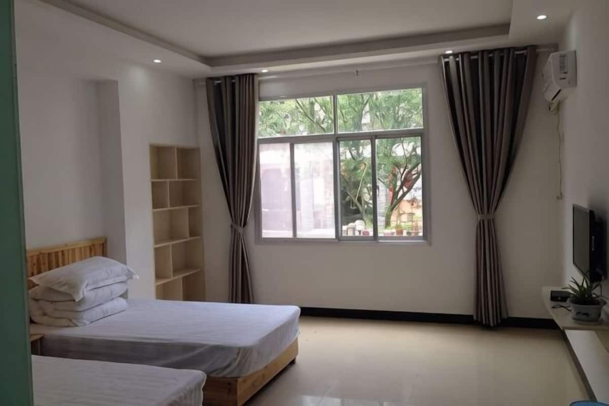 A bedroom with two beds, a window, a TV, and a shelf.