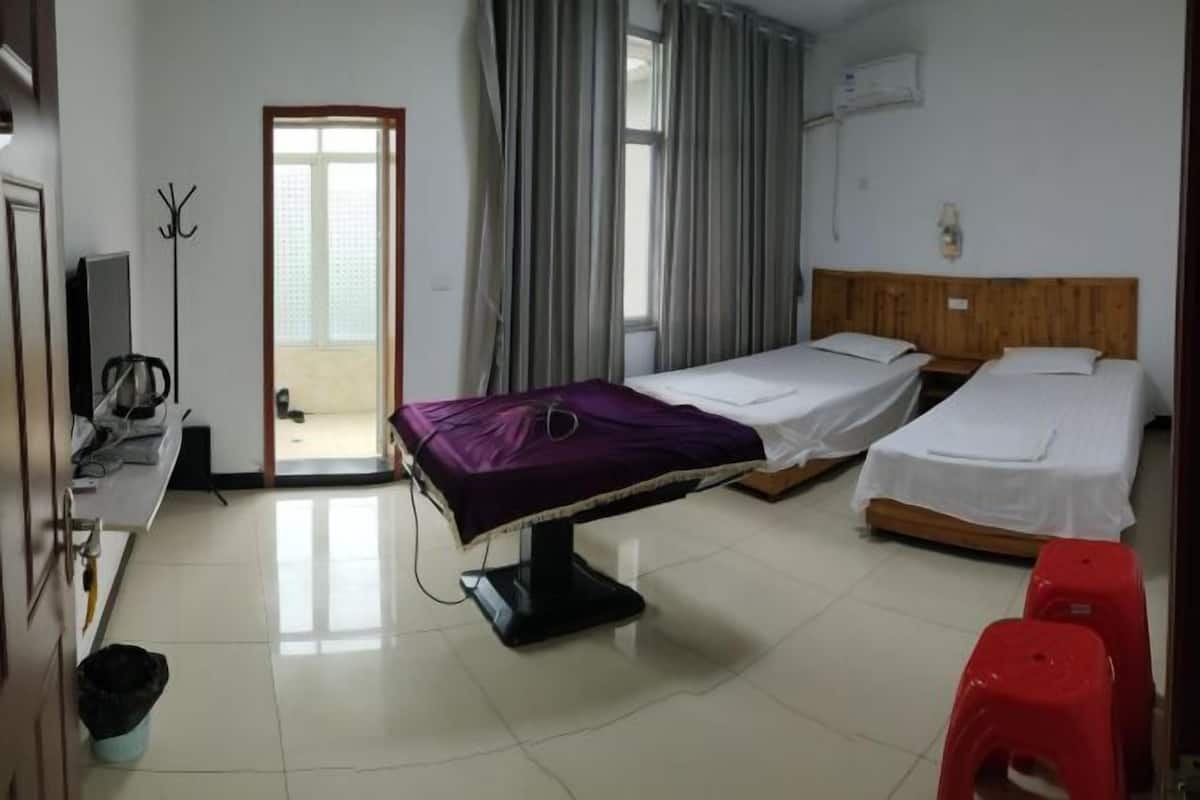 A hotel room with two single beds, a desk with a chair, a coat rack, and a television.