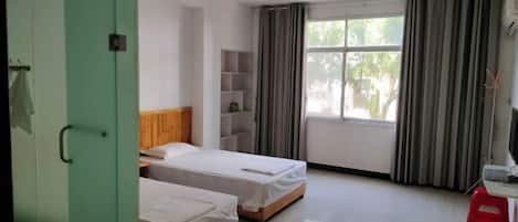 Quarto com duas camas, uma escrivaninha, uma janela com cortinas e uma porta verde.
