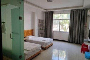 Una habitación con dos camas, un escritorio, un ventanal con cortinas y una puerta verde.