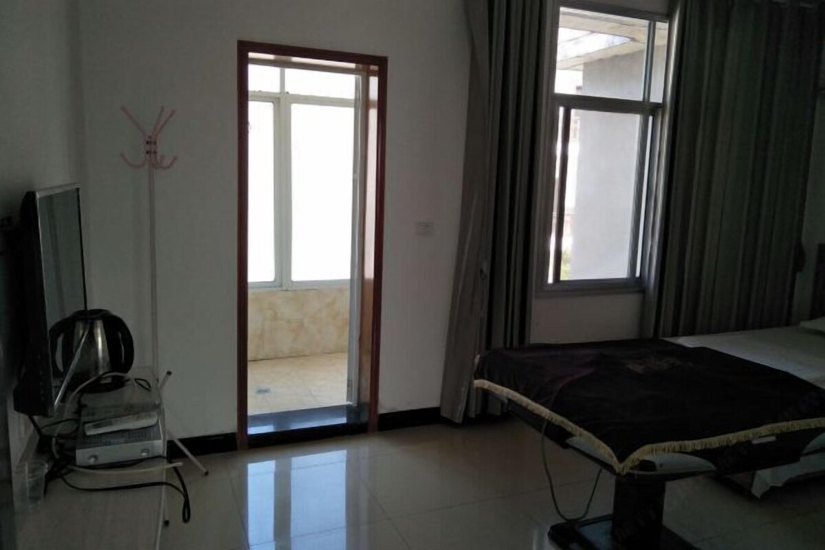 Una habitación de hotel con cama, televisión, escritorio con silla y ventana con cortinas.
