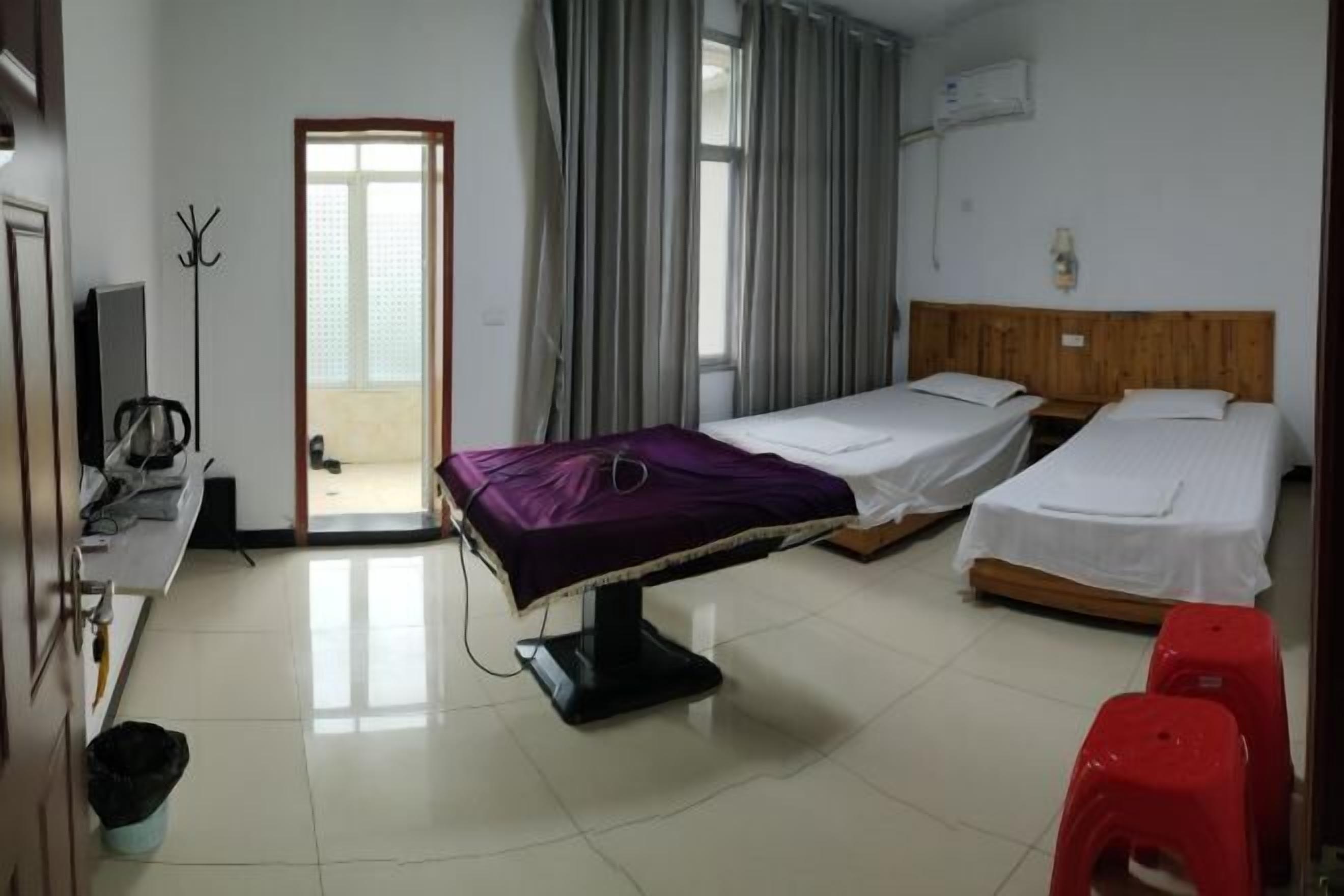 A hotel room with two beds, a TV, a coat rack, and a window with curtains.