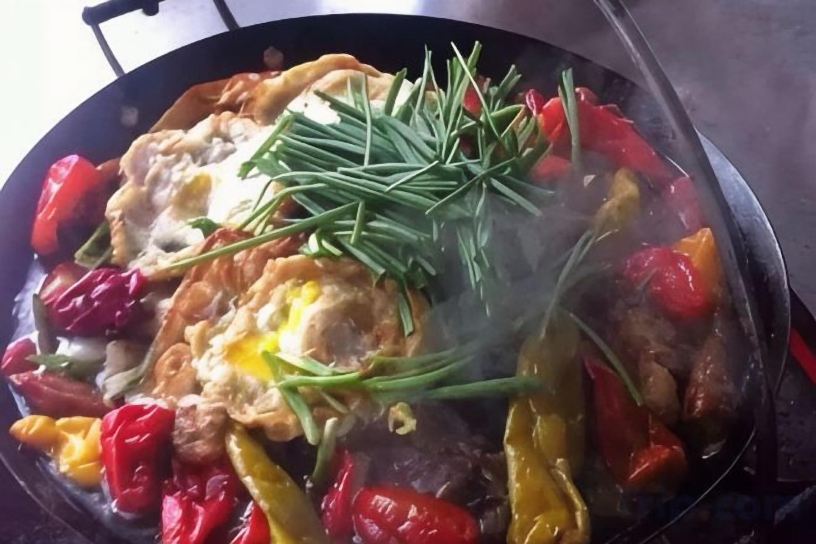 Eine Pfanne mit Eiern, roten und gelben Paprika und grünen Kräutern auf einem Herd.