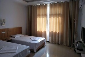 Habitación de hotel con dos camas, cabecera de madera, mesita de noche, lámpara y ventana con cortinas.