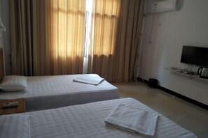 Una habitación de hotel con dos camas, un televisor sobre un soporte y una ventana con cortinas.