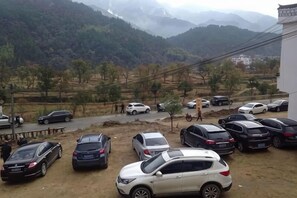 Un estacionamiento con varios coches, un sendero de tierra y montañas al fondo.