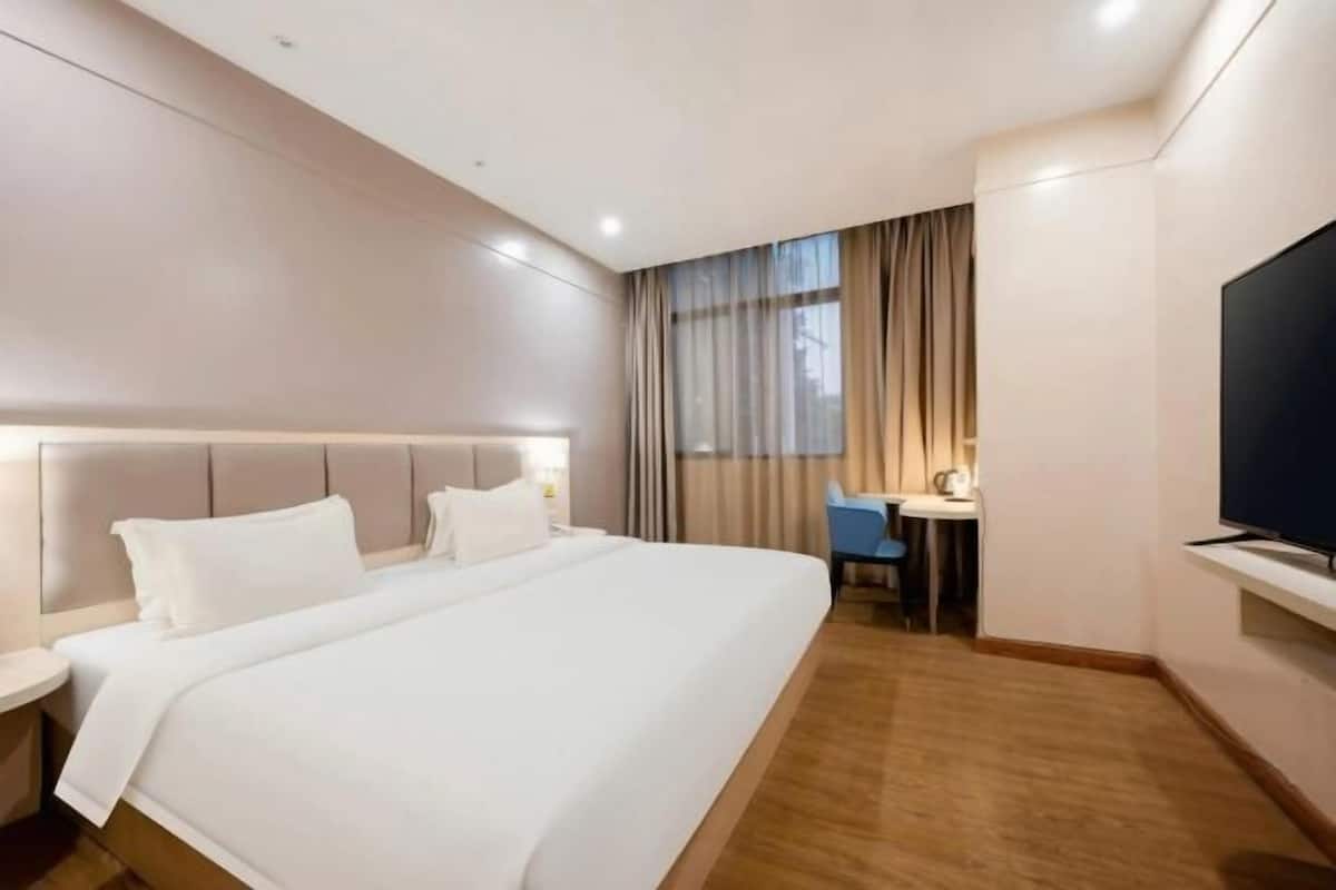 A hotel room with a large bed, a desk, a chair, a TV, and a window with curtains.