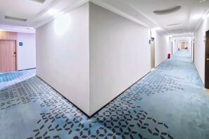 A hotel corridor with a patterned carpet, white walls, and doors on both sides. - 7 Days Premium (Zhongshan)