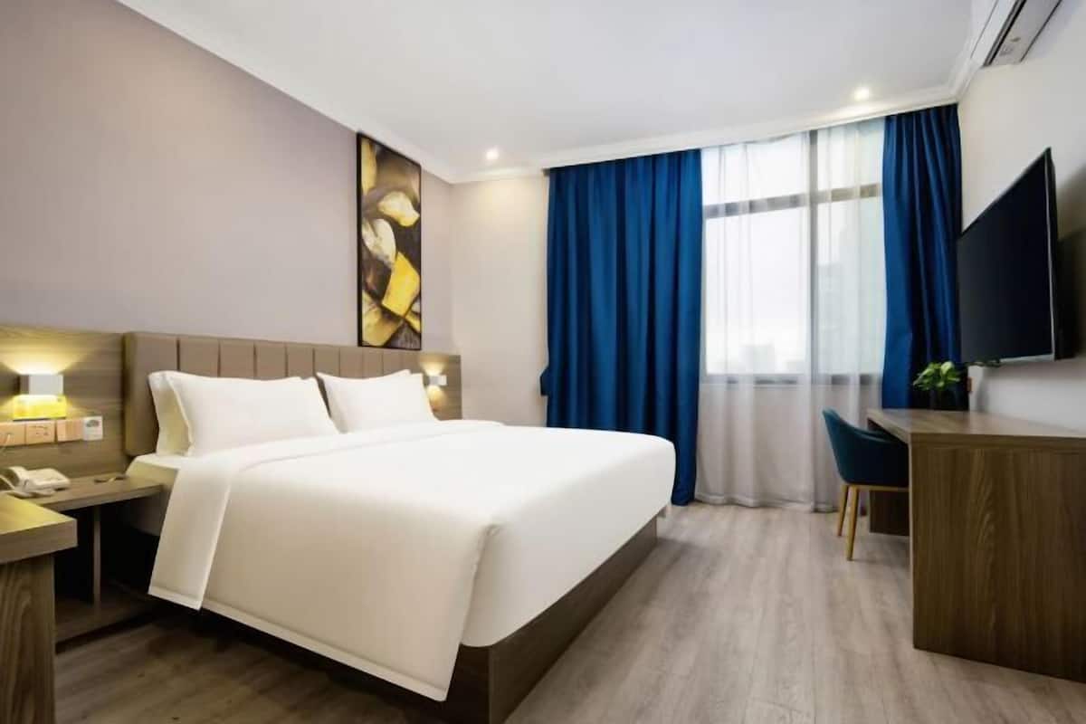 A hotel room with a bed, bedside table, desk, chair, TV, and curtains.
