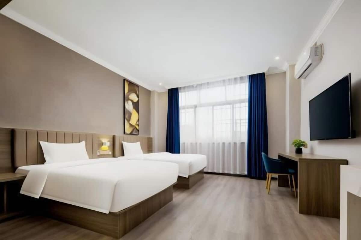 A hotel room with two beds, a desk, a chair, a TV, and a window with curtains.
