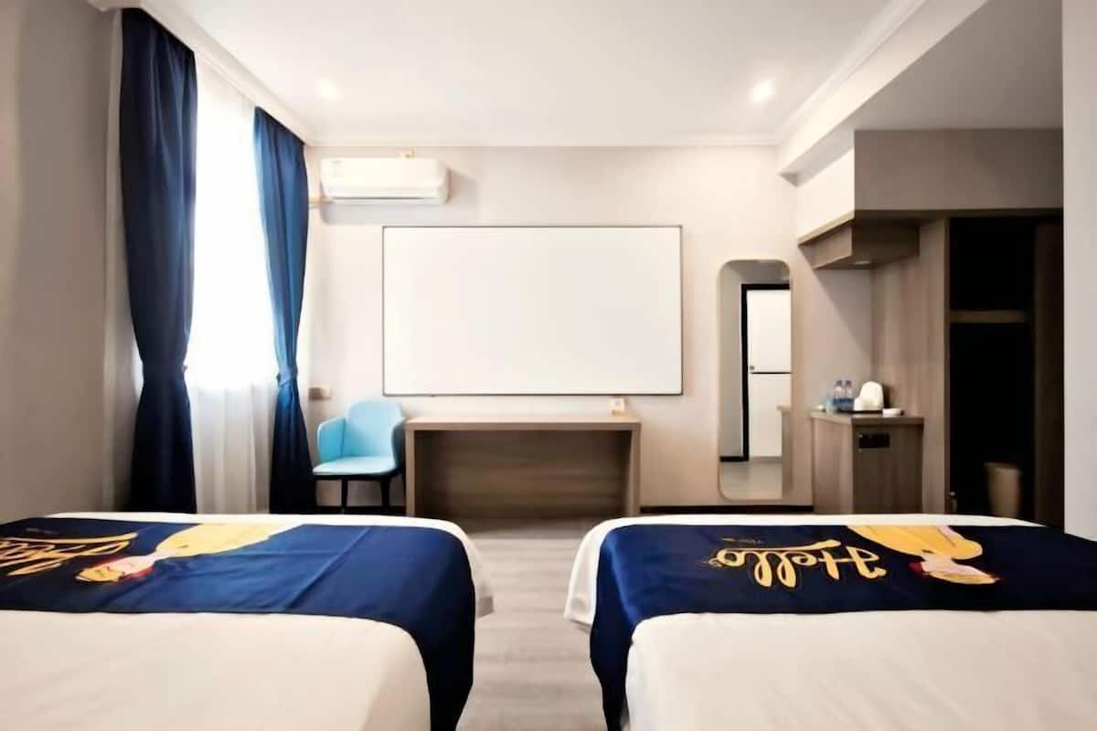 A hotel room with two beds, a desk, a chair, a mirror, and a wardrobe.