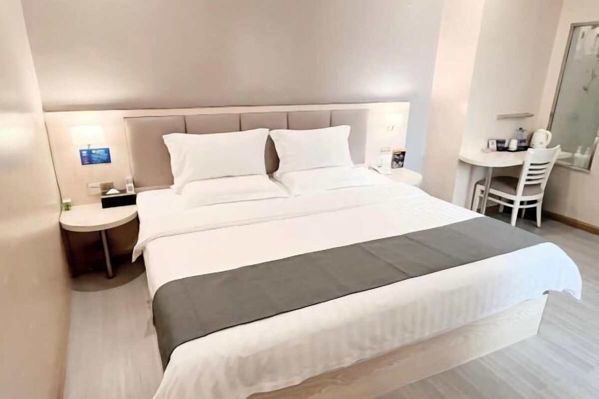 A hotel room with a bed, bedside table, and a desk with a chair.