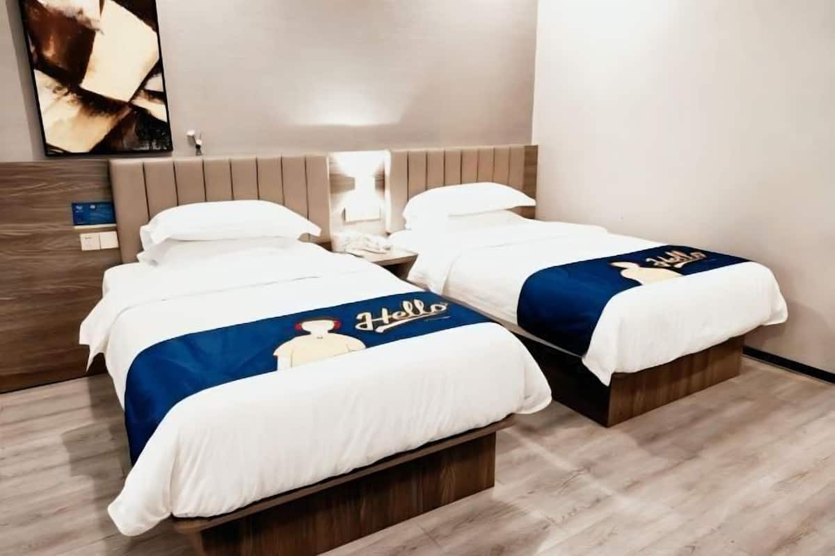 A hotel room with two beds, each with a white and blue bedspread, a wooden headboard, a nightstand, and a wall-mounted artwork.