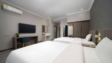 A modern hotel room with two beds, a desk, a flat-screen TV, and a small seating area.