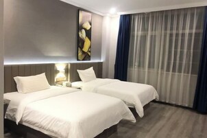 Habitación de hotel con dos camas, un ventanal con cortinas translúcidas y una obra de arte colgada en la pared.