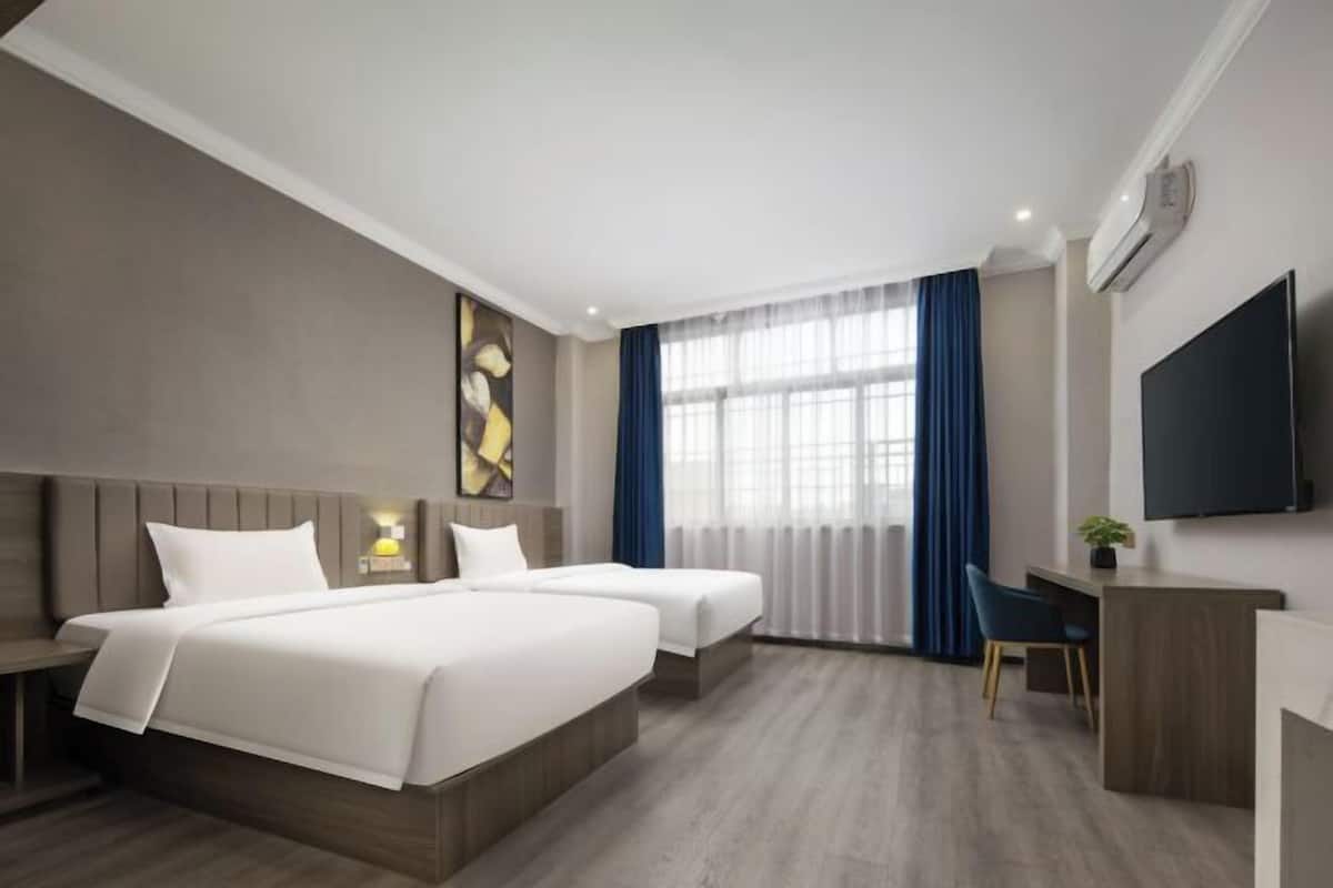 A hotel room with two beds, a desk, a chair, a TV, and a window with curtains.