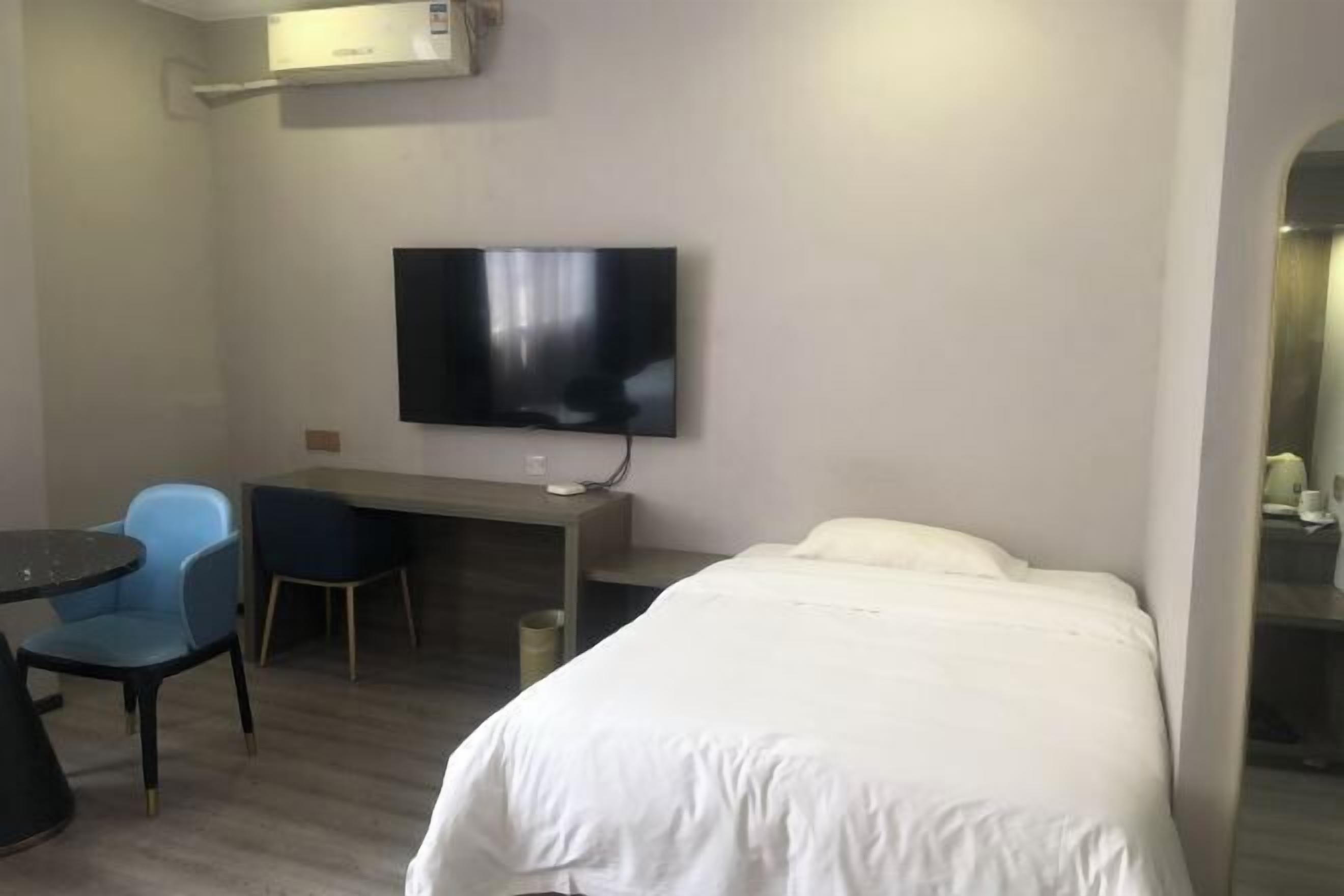 A hotel room with a bed, a desk, a chair, a television, and an air conditioning unit.