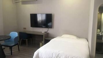 A hotel room with a bed, a desk, a chair, a television, and an air conditioning unit.