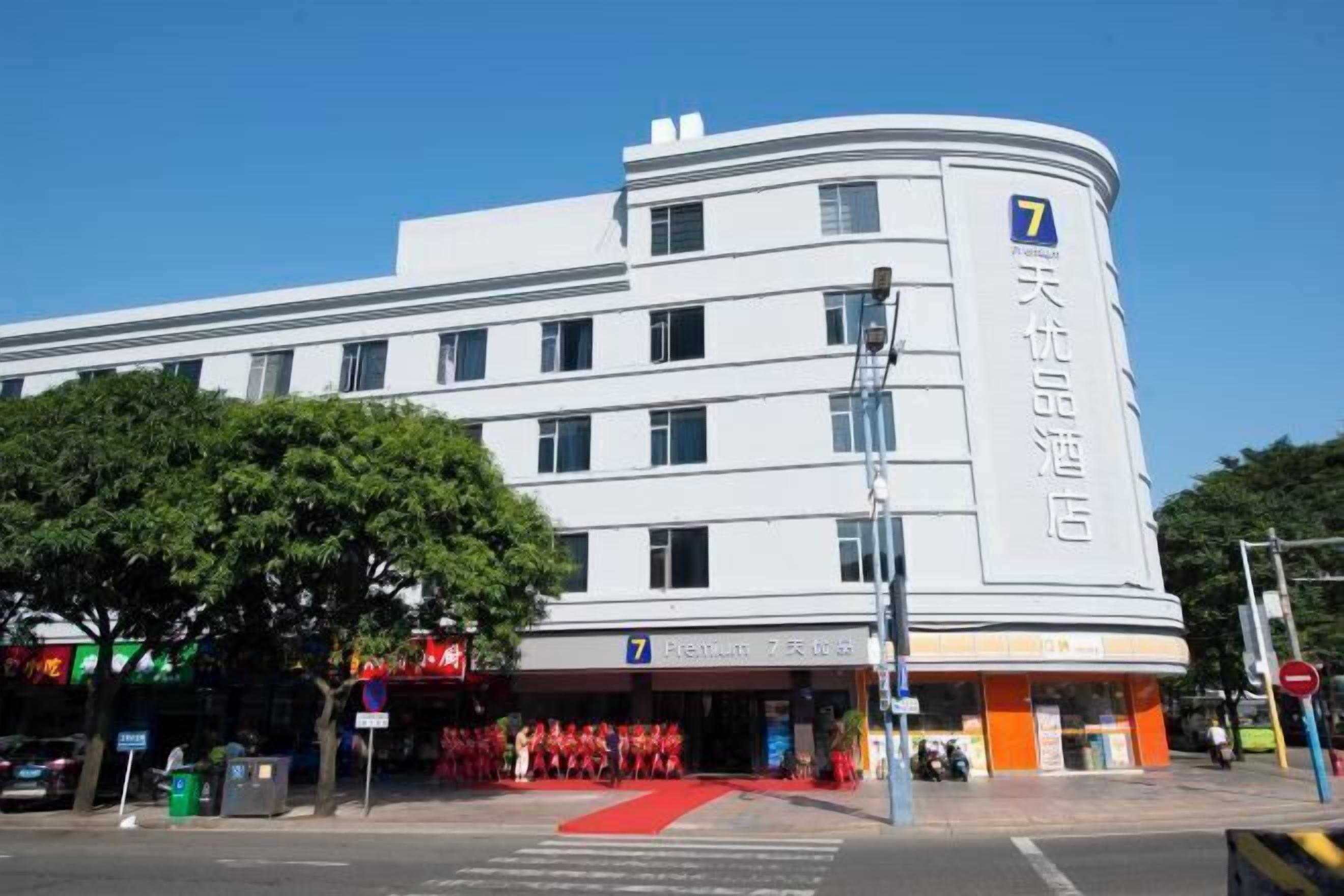 A white hotel with a prominent number '7' on the facade, a red carpet entrance, and a clear blue sky in the background.
