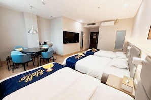 A hotel room with two beds, a desk, chairs, a TV, and a minibar.