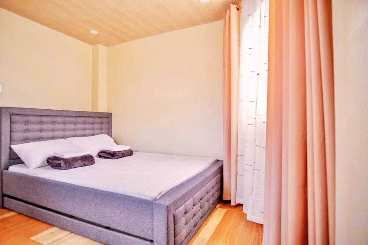 Un dormitorio con una cama tapizada en gris, ropa de cama blanca y suelo de madera.