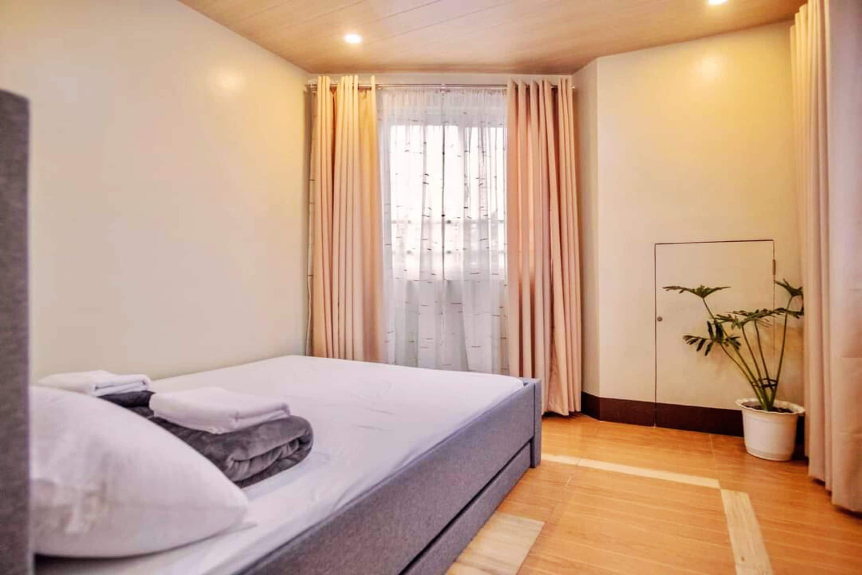 A bedroom with a bed, curtains, a potted plant, and a wardrobe.