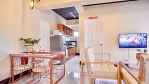 A modern living room with a dining area, a kitchen, and a TV mounted on the wall.