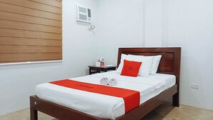 A hotel room with a wooden bed, white bedding, a red pillow, and a towel on the bed. - Reddoorz @ David's Travellers Inn Cavite (General Trias)