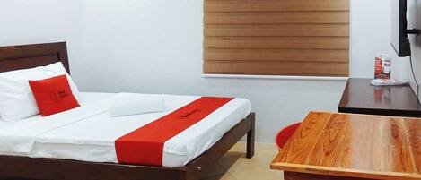 A hotel room with a bed, a wooden table, a chair, a TV, and a window with blinds.