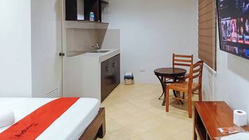 Ein kompaktes Hotelzimmer mit Bett, einer kleinen Küchenzeile, einem Esstisch mit Stuhl und einem an der Wand befestigten Fernseher.