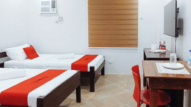 A hotel room with two beds, a desk, a chair, a TV, and a window with blinds. - Reddoorz @ David's Travellers Inn Cavite (General Trias)