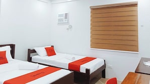 A hotel room with two single beds, a wooden desk, a chair, a window with blinds, and a wall-mounted air conditioning unit. - Reddoorz @ David's Travellers Inn Cavite (General Trias)