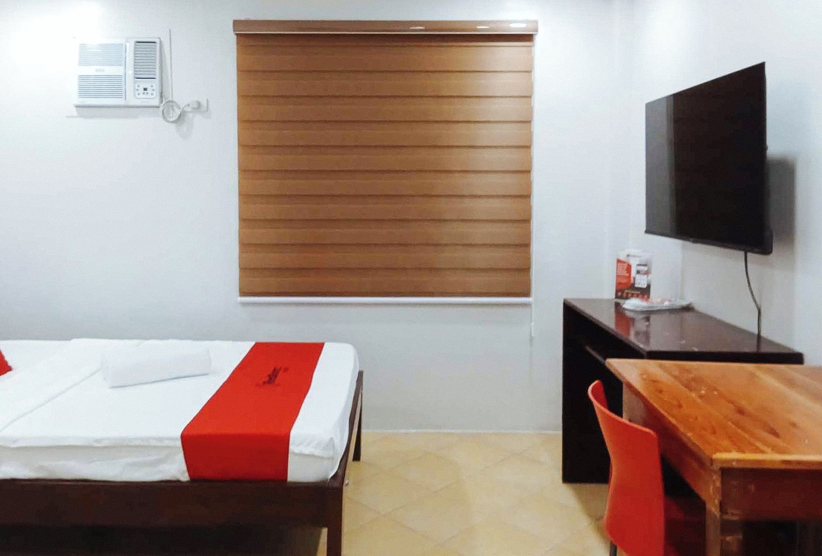 A hotel room with a bed, a desk, a chair, a TV, and a window with blinds.