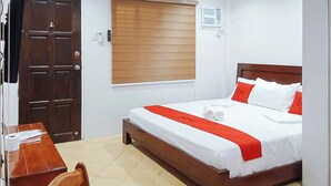A hotel room with a wooden bed, white bedding, a red accent, a wooden desk, and a chair. - Reddoorz @ David's Travellers Inn Cavite (General Trias)