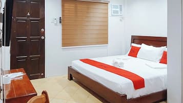 A hotel room with a wooden bed, white bedding, a red accent, a wooden desk, and a chair.
