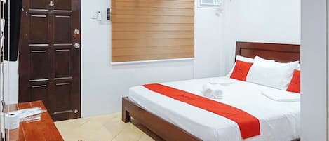 Una camera d'albergo con un letto in legno, biancheria bianca, un tocco di colore rosso, una scrivania in legno e una sedia.